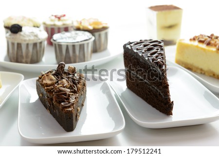 Close up of assorted cake slices and cupcakes served on white plates
