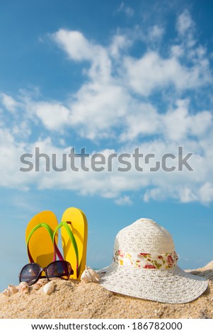 Yellow flip flop, sunglasses and floppy hat at the beach
