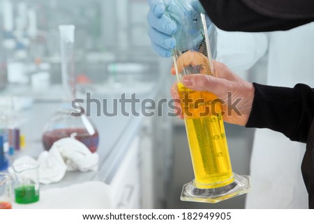 A Chemist is using a yellow filled graduated cylinder in her laboratory.