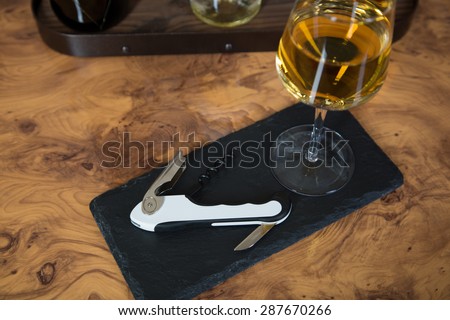A vine bottle opener on a roof slate with a glass of white wine.
