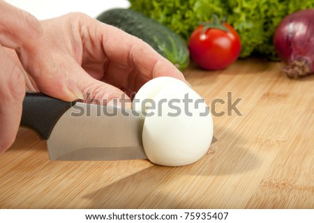 A woman is cutting an egg in preparation for a salad.