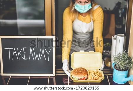 Young woman preparing takeaway food inside restaurant during Coronavirus outbreak time - Worker inside kitchen cooking fast food for online order service - Focus on hamburger