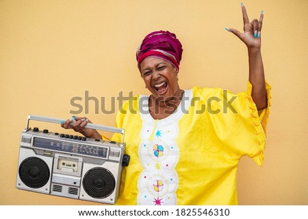 Happy senior black woman with traditional african dress dancing holding vintage stereo - Focus on face