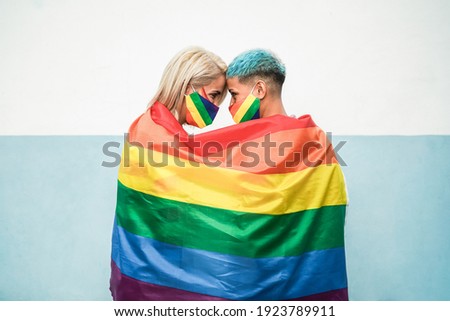 Young couple of lesbian women under lgbt rainbow flag wearing masks at gay pride parade - Focus on faces