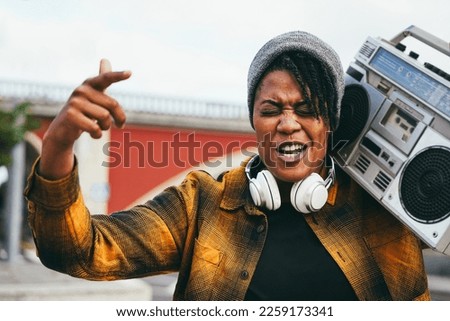 African woman singing and listening music from vintage boombox stereo with city in background - Focus on face Stock fotó © 
