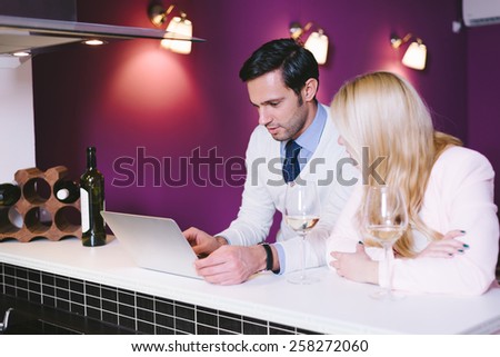Young couple in the kitchen, drinking wine, and looking at laptop, vintage style filtered look
