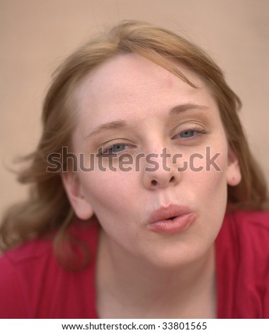 A pretty young woman looks at the viewer with perched lips blowing air or a kiss at the camera