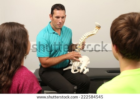 A Chiropractor showing a model of the human spine to two children