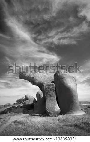 A wind sculpted rock formation in a field set against a dramatic sky.  Black and white.