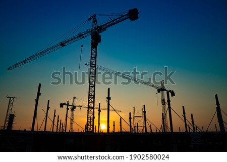 New construction site with cranes on orange sunset, sunrise sky background. Steel frame structure, structural steel beam build large buildings at construction site . construction machinery.