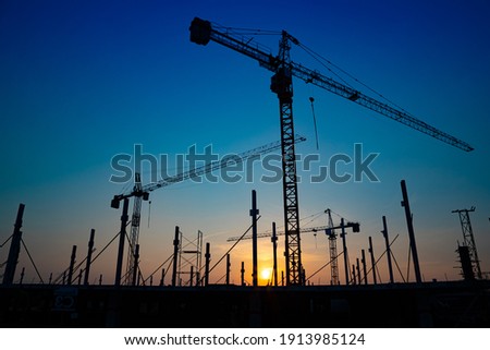 Construction site with cranes on orange sunset, sunrise sky background. Steel frame structure, structural steel beam build large buildings at construction site . construction machinery.