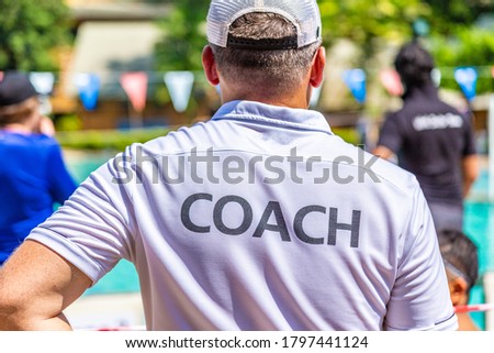 Male swimming coach in white COACH shirt standing in the sun watching his swimmers competing in the pool on a bright sunny day Photo stock © 