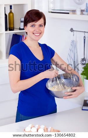 Young happy brunette woman preparing dough for a cake in a kitchen