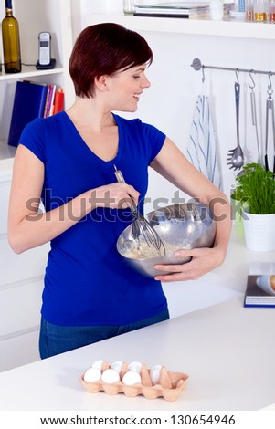 Young happy brunette woman preparing dough for a cake and checking the receipe