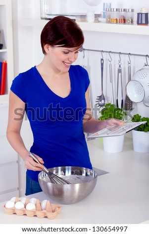 Young happy brunette woman preparing dough for a cake and checking the receipe on a tablet pc