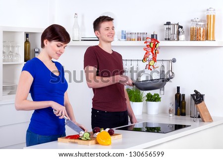 young woman chopping vegetables and man flipping food in the pan