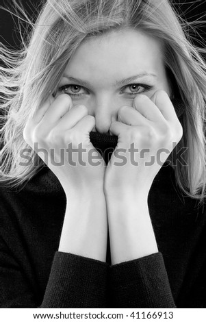 beautiful blonde girl covers her mouth with a black turtleneck on black background (black and white image)