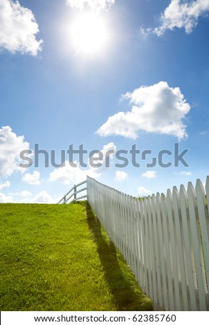 white fence, blue sky, green grass, clouds and the sun