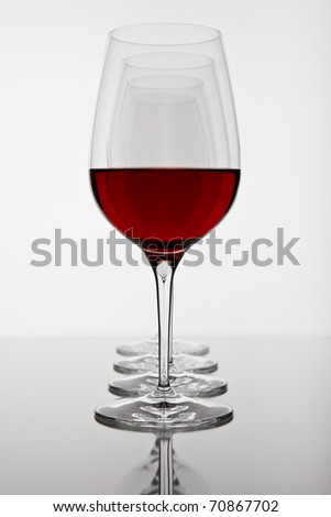 a row of four wine glasses, the first on filled with red wine