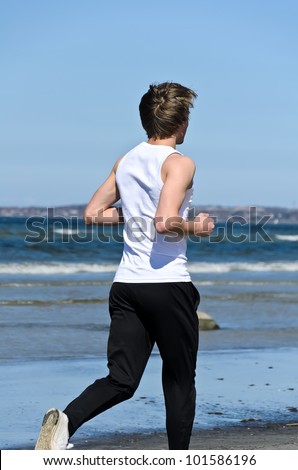Athletic young male running on the beach. From the back
