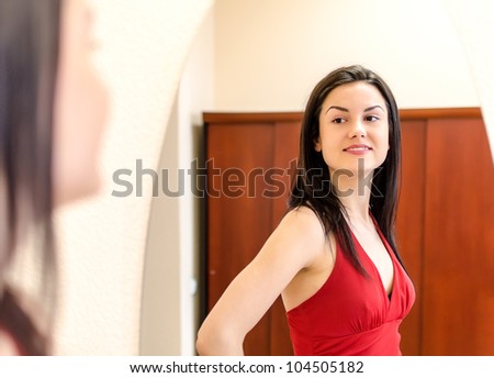 Beautiful smiling girl in red dress posing in front of a mirror