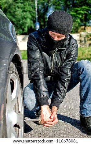 Man in mask punctures a car tyre. Revenge concept