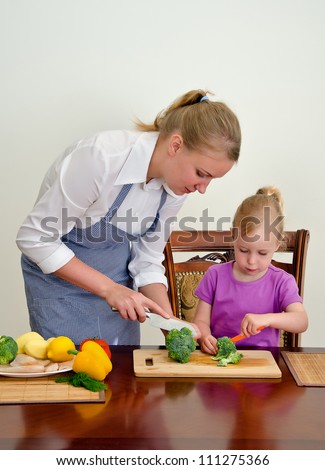 Mother and daughter preparing food. Cutting broccoli with knife.