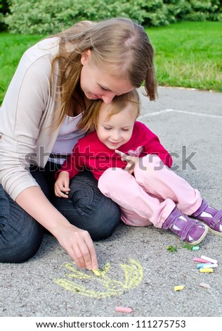 Mother and daughter drawing with chalk on asphalt