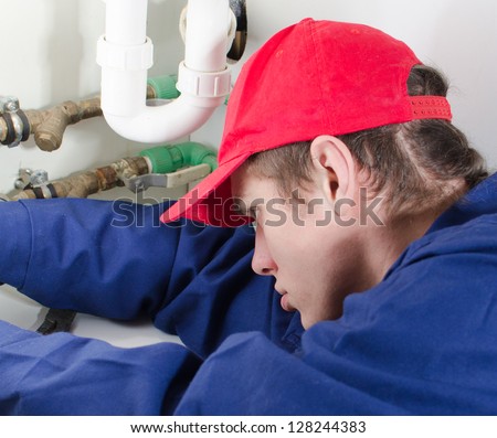 Rear view of plumber in uniform repairing pipeline in the house.