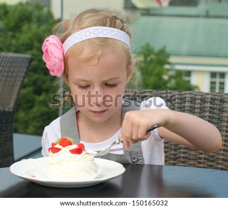 Cute little girl eating cake in outdoor cafe