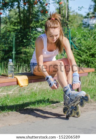 Pretty girl sitting on the bench and putting on inline skates.