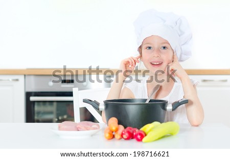 Little girl in chef hat cooking in kitchen.