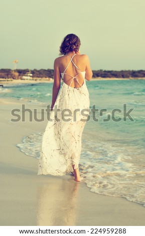 Woman in white dress walking on the beach.