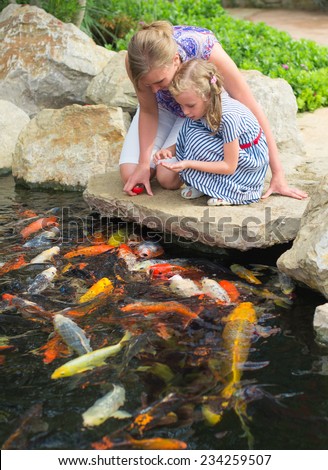 Woman and daughter feeding fishes in pond.