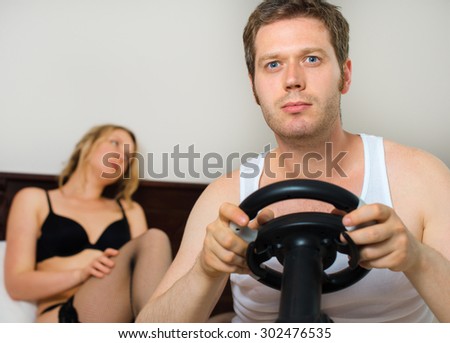 Video game addiction. Man playing video game with steering wheel, upset woman on background.