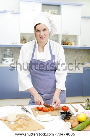 Attractive chief cook preparing food, cutting tomatoes