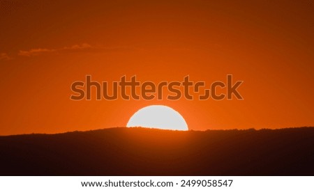 Similar – Image, Stock Photo Behind the hill with plants, a bright glow appears against the already darkened sky. The sun sets on the horizon.