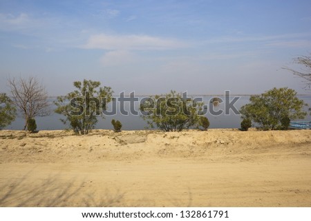 Indian landscape with shrubs growing between a sandy track and the lagoons of the wetland nature reserve at Harike near Amritsar in the Punjab