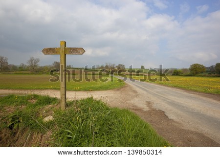 yorkshire wolds scenery with agricultural fields and a wooden public footpath sign under a cloudy blue sky in springtime