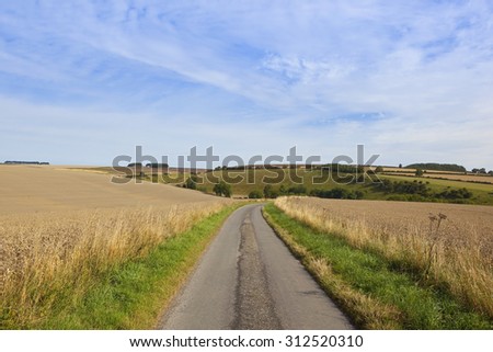 a small countryside road on the yorkshire wolds england with views of patchwork farmland under a blue sky in late summer