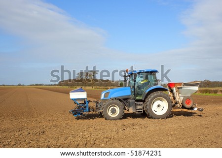 a blue tractor applying pesticides and cultivating soil in springtime under a blue sky