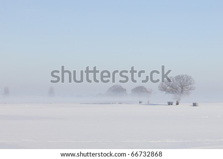 a simple background landscape with snow covered fields and distant trees half obscured by mist under a clear blue sky