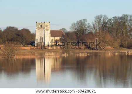 an english winter landscape with flooded fields trees and an ancient stone church under a blue sky
