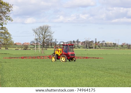 a red crop sprayer in green fields of wheat in springtime under a cloudy blue sky