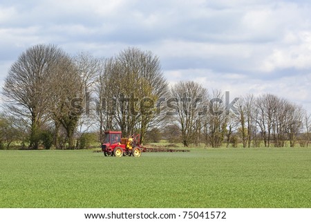 a red crop sprayer in green fields of wheat in springtime under a cloudy blue sky