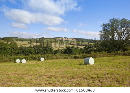 a summer landscape with plastic wrapped hay bales and a view of the patchwork fields trees and hedgerows of the yorkshire wolds