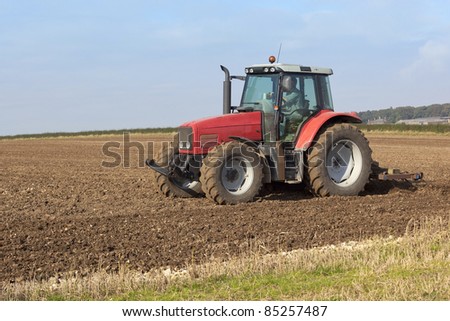 a red tractor cultivating fields on a hillside in autumn