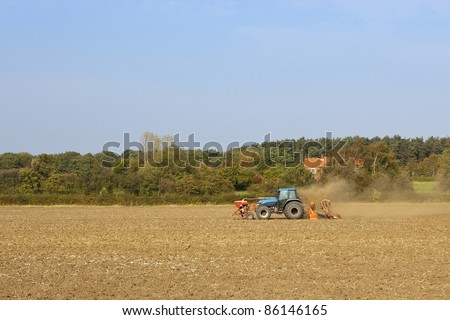 an autumn agricultural landscape with soil patterns and textures and a blue tractor under a blue sky
