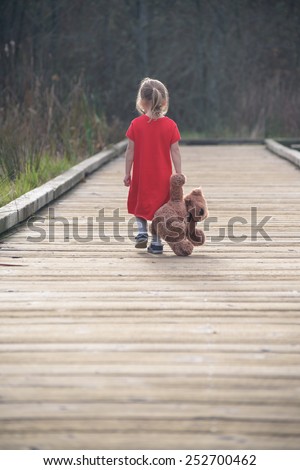 Sad girl walking on wooden path with teddy bear, view from behind