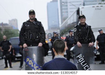 TORONTO-JUNE 26:   A peaceful protester meditating on the streets and being watched closely by riot officers during the G20 Protest on June 26, 2010 in Toronto, Canada.